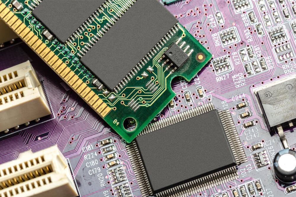 Mão de técnico instalando ou removendo módulo de memória RAM verde em um circuito interno de notebook.