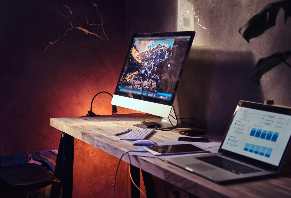 Computador all in one e notebook em mesa de home office com teclado, mouse e acessórios.