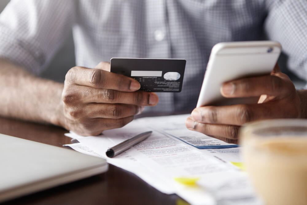 Pessoa segurando cartão de crédito e celular para contestar compra não reconhecida